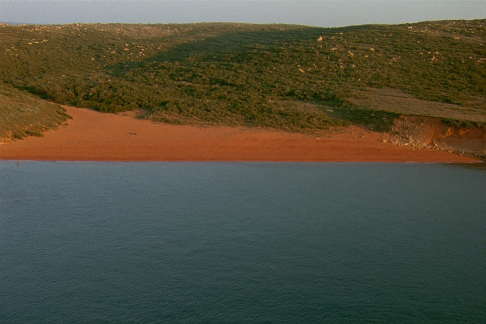 Ramla Bay on Gozo at golden hour, a wide beach of reddish-gold sand in a green valley