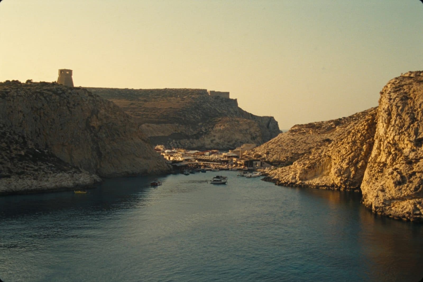 Xlendi Bay on Gozo at golden hour, a narrow inlet between limestone cliffs